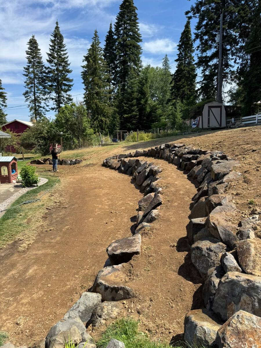 Curved natural rock retaining wall on residential hillside in North Idaho by Elkry Construction